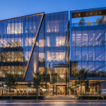 Contemporary mixed-use building with dramatic angular Glass Facade Architecture and illuminated curtain wall glazing at dusk