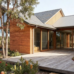 Single storey house facade ideas – warm earthy natural timber cladding with stone pillars, wide timber deck, sliding glass doors and native garden, Daylesford VIC