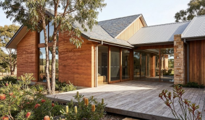 Single storey house facade ideas – warm earthy natural timber cladding with stone pillars, wide timber deck, sliding glass doors and native garden, Daylesford VIC